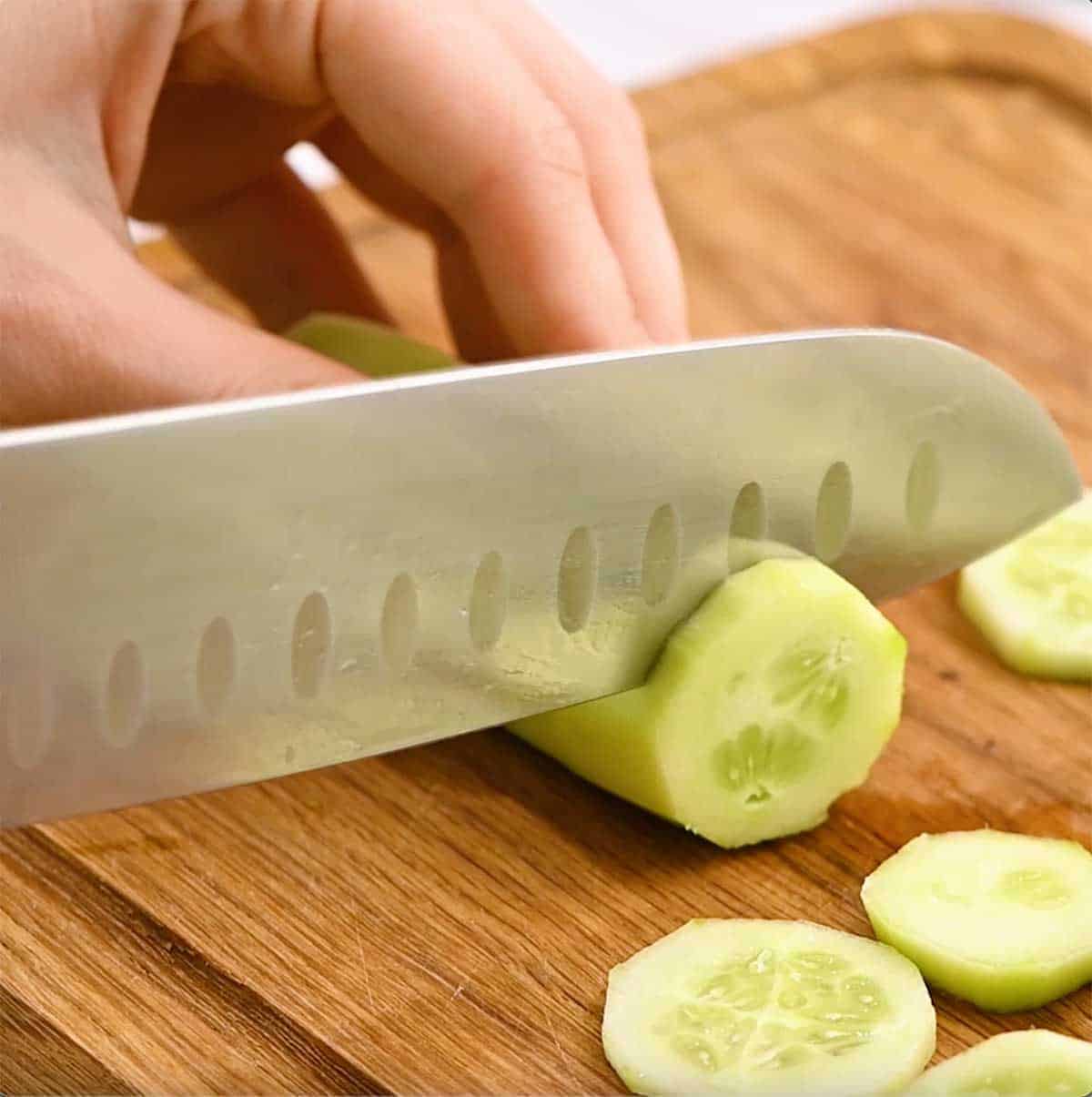 peeled cucumber being sliced with a large knife