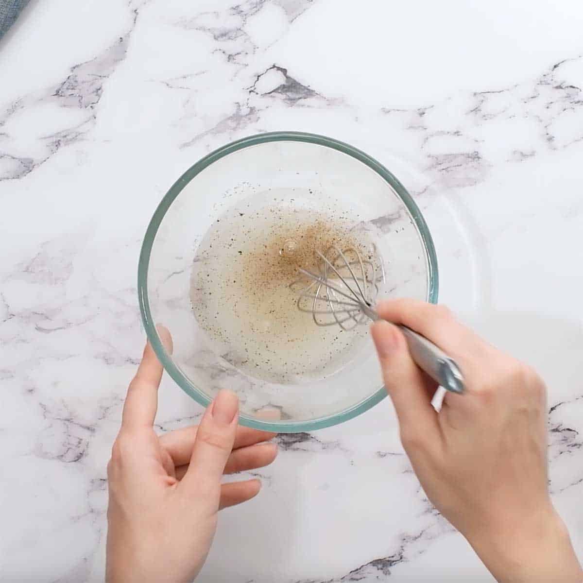 glass bowl with vinegar, water, sugar, salt, and pepper being whisked together