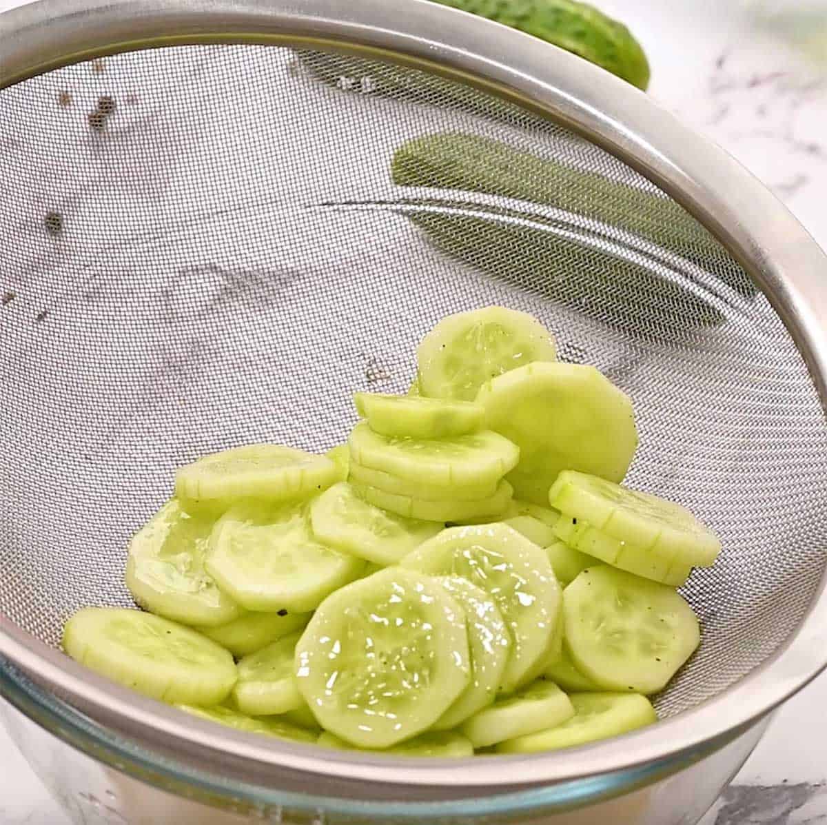 draining marinated cucumbers in a metal strainer
