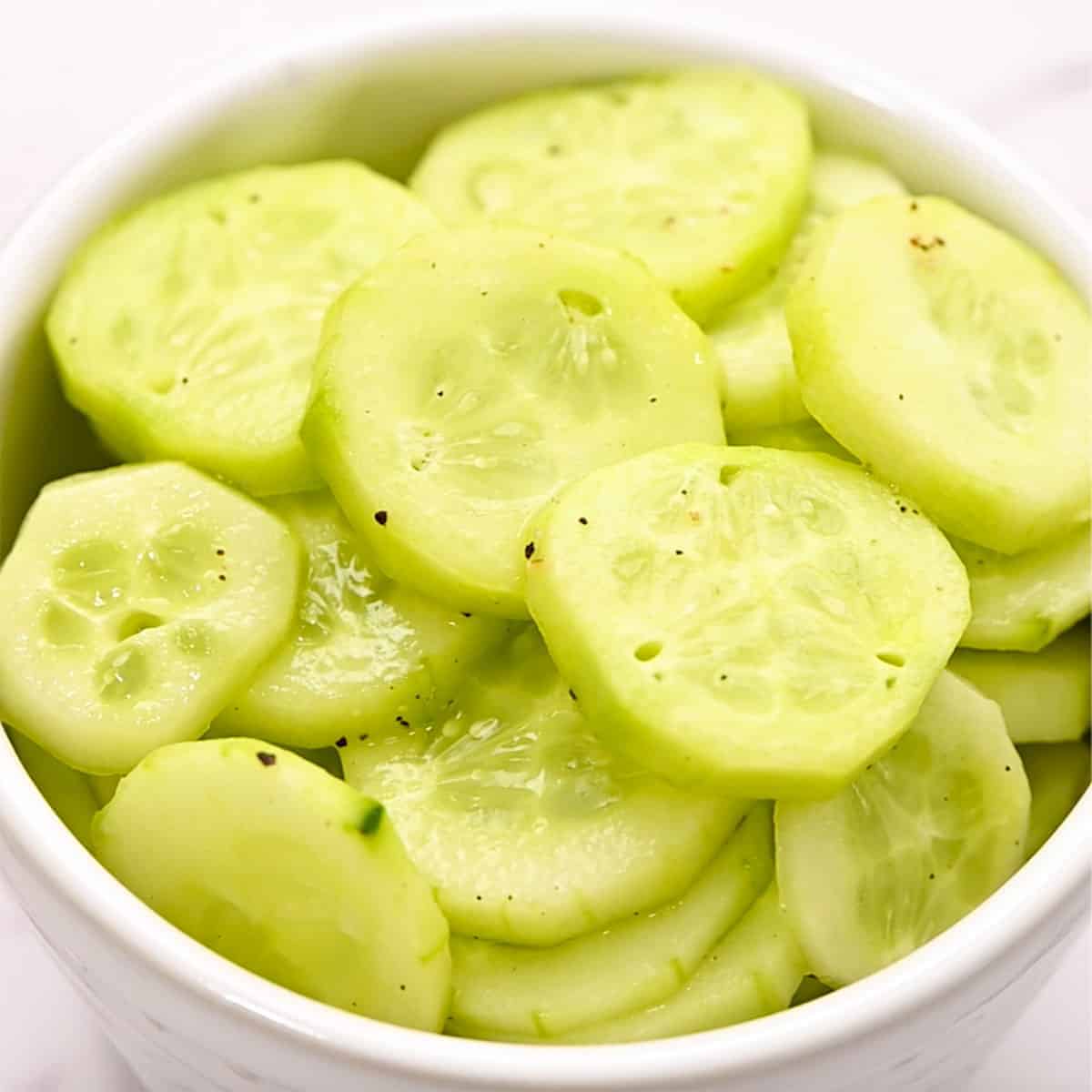 white bowl full of peeled, sliced, marinated cucumbers