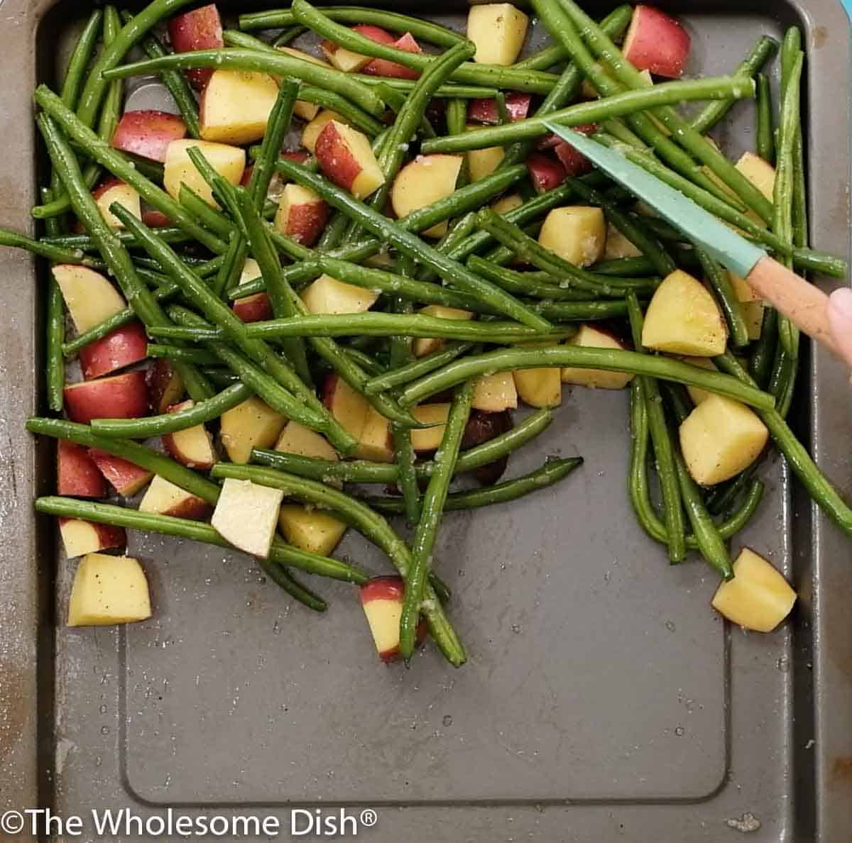 chopped red potatoes and green beans on a baking sheet with seasonings ready to cook