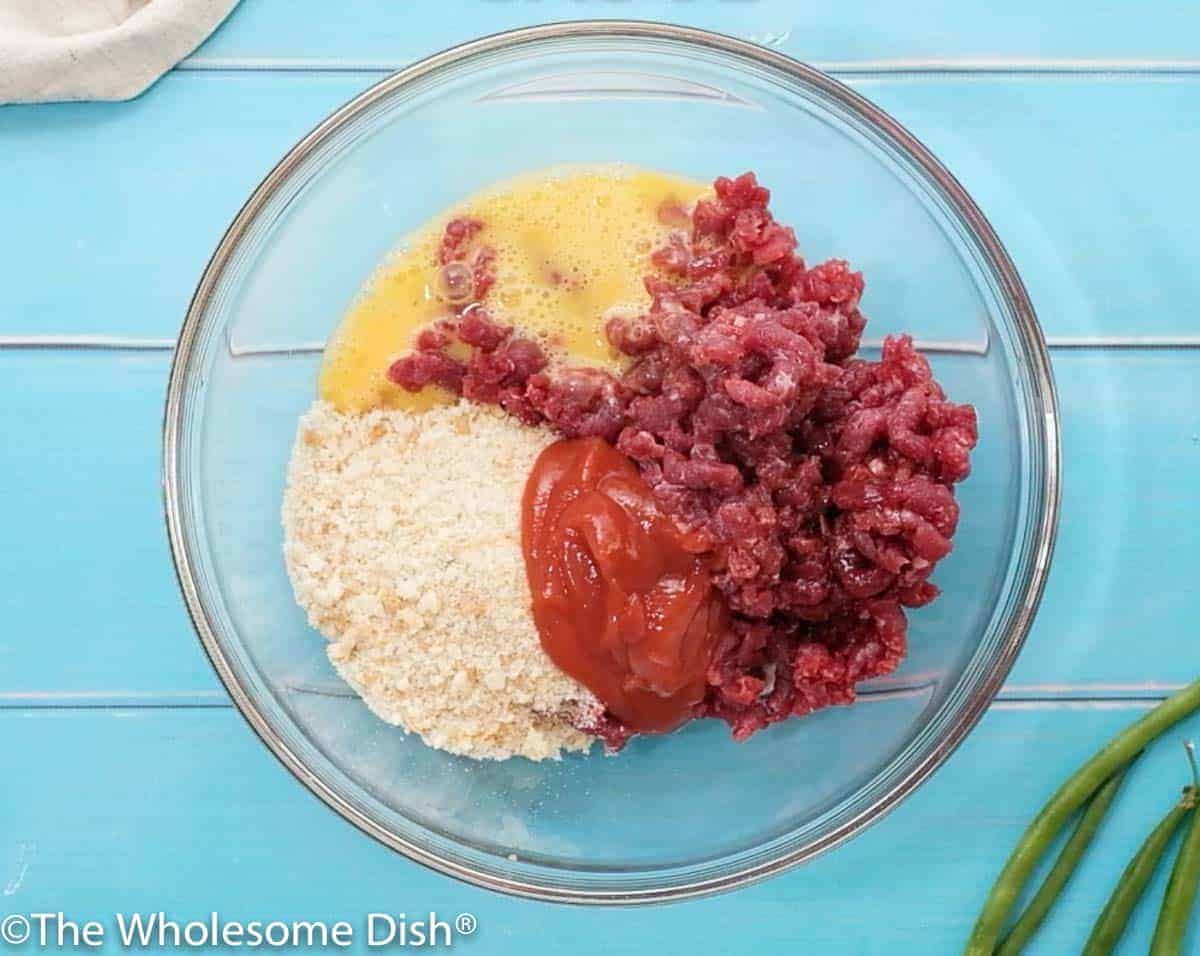 mixing bowl full of ground beef, breadcrumbs, an egg, ketchup, and Worcestershire sauce