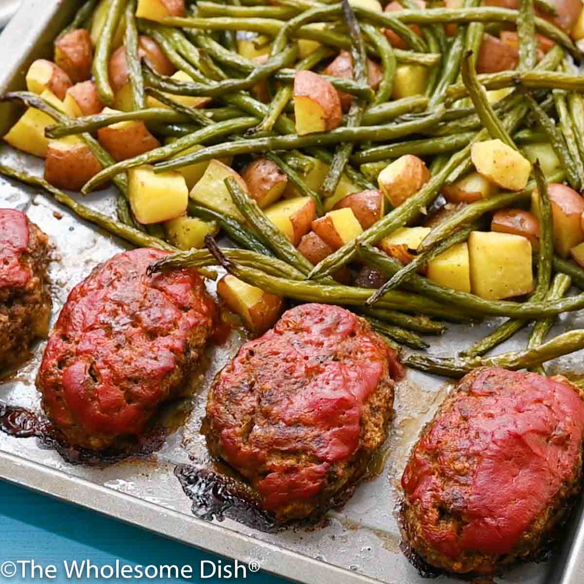 cooked meatloaf, potatoes, and green beans on a sheet pan