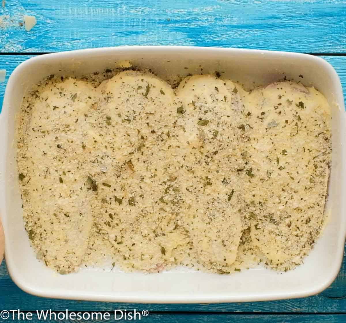 mayo, parmesan, and breadcrumbs sprinkled over uncooked chicken in a baking dish