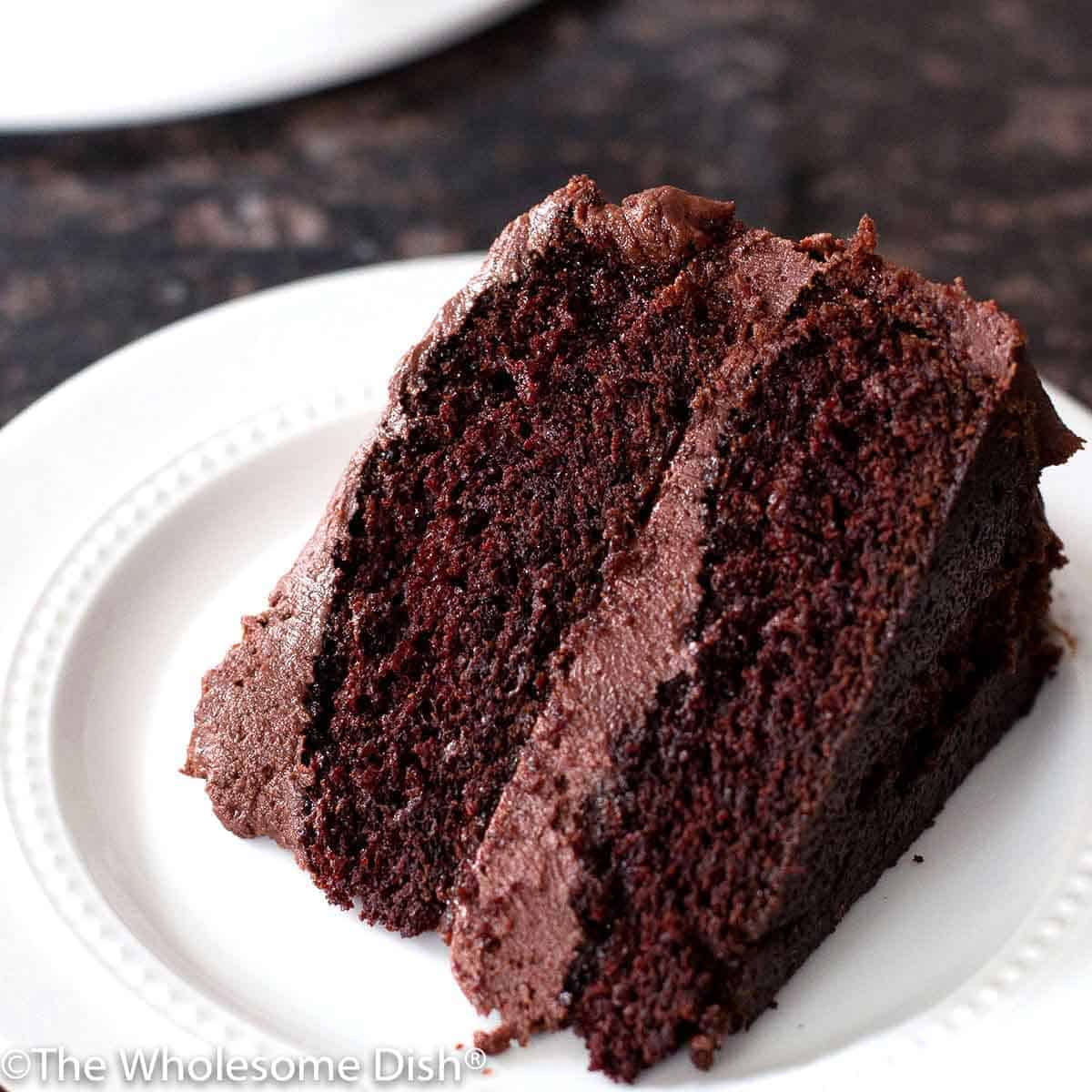 slice of homemade chocolate cake with chocolate frosting on a white plate