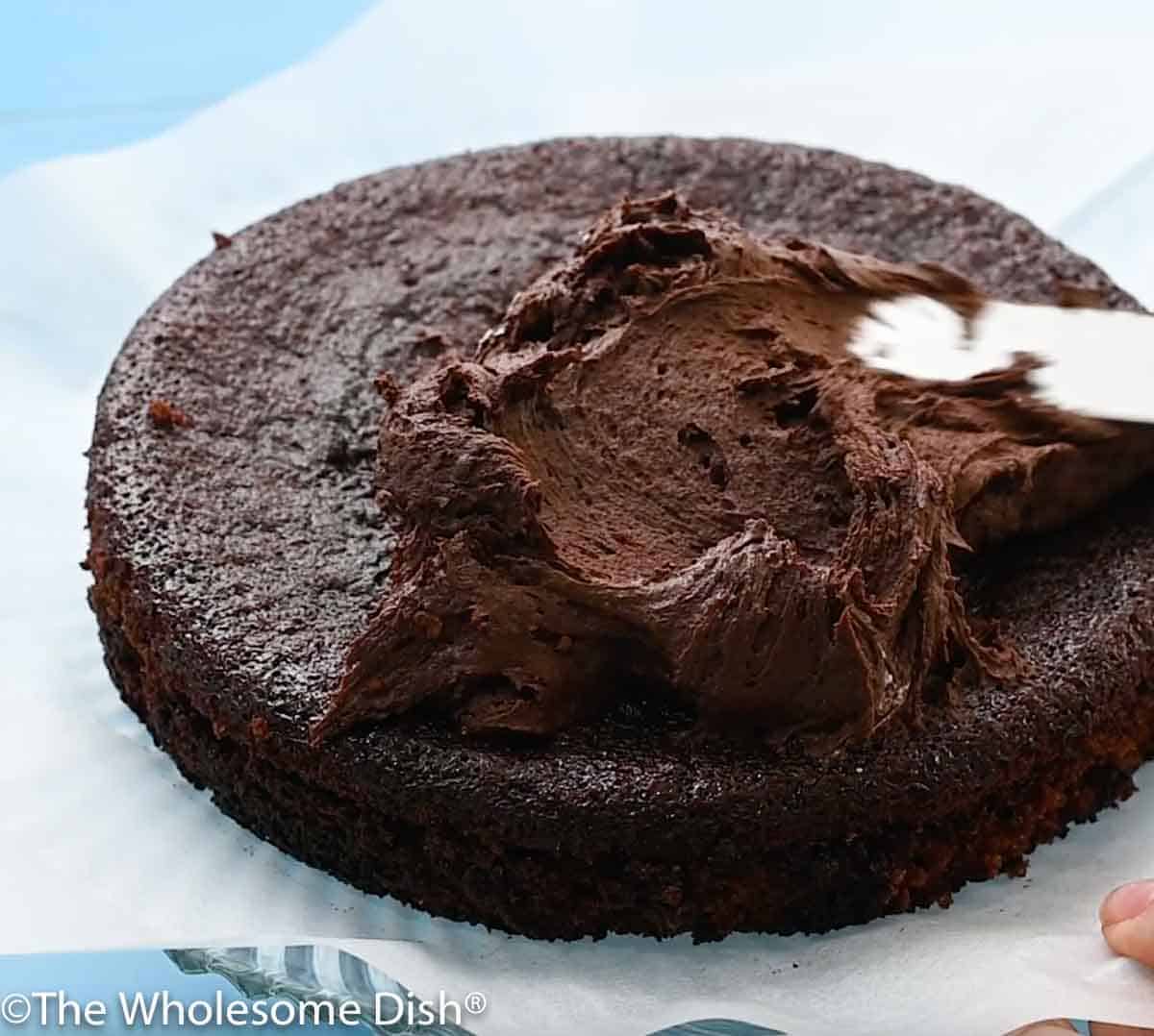 spreading chocolate frosting on a round chocolate cake