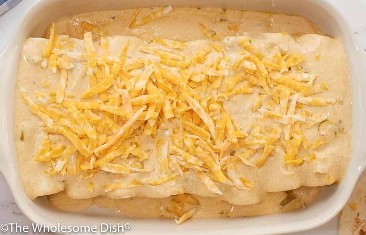 Shredded cheese sprinkled over sour cream enchiladas