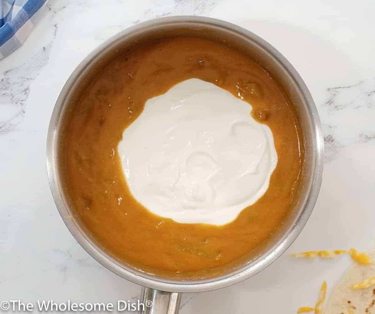 Sour cream being added to white enchilada sauce
