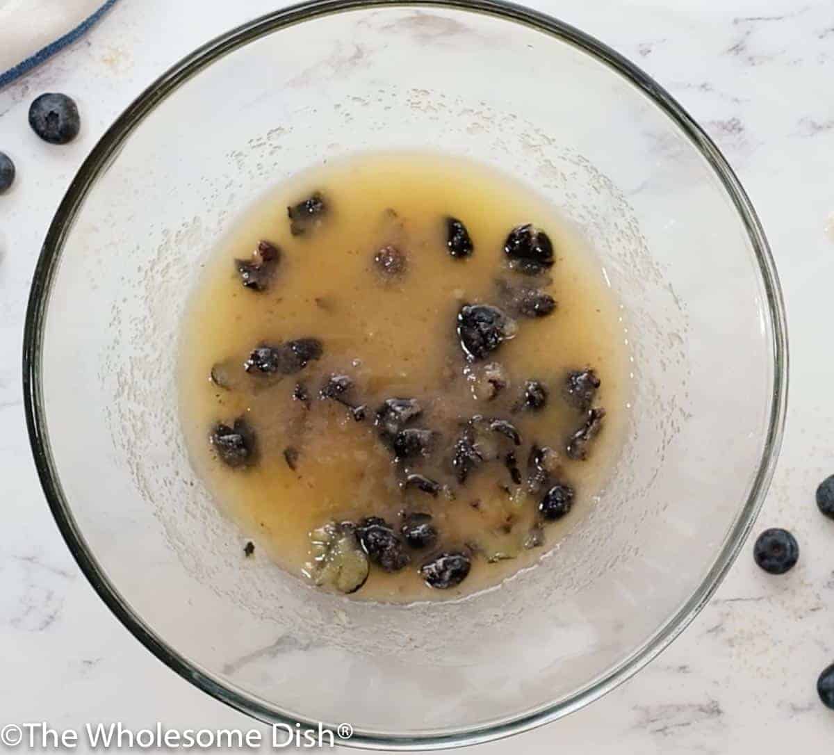 Mixing bowl with smashed blueberries, melted butter, and sugar.