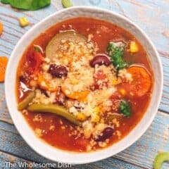 White bowl full of crock pot minestrone soup topped with parmesan cheese.