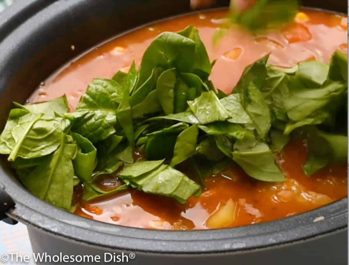 Adding spinach to the slow cooker.