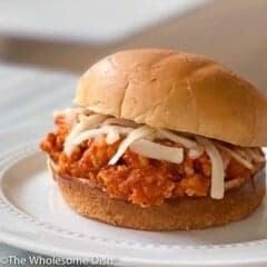 Chicken parmesan sloppy joe on a bun topped with mozzarella on a white plate.