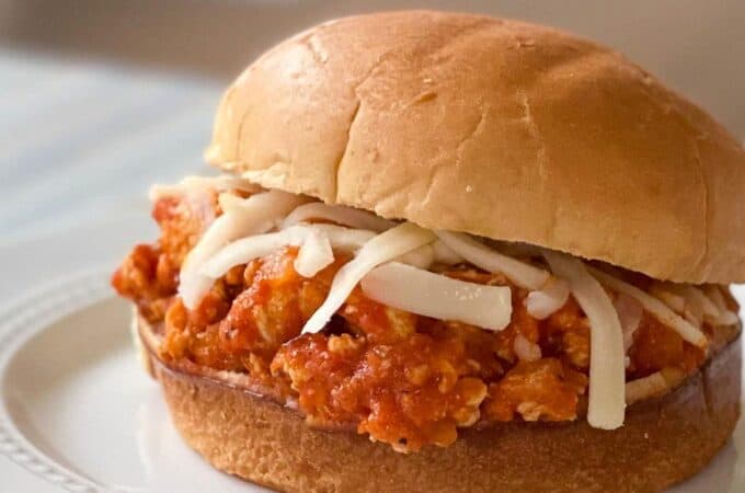 Chicken parmesan sloppy joe on a bun topped with mozzarella on a white plate.