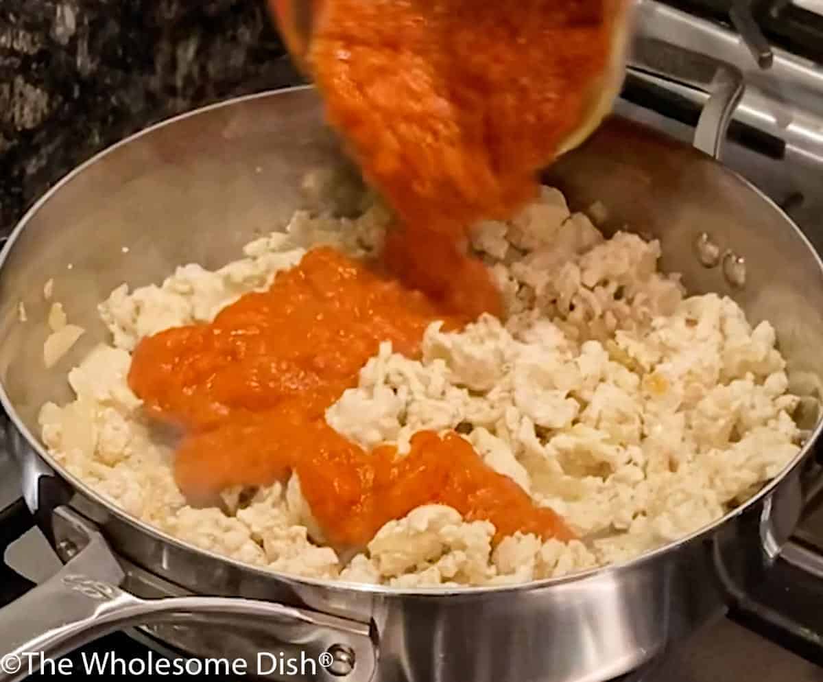 Pouring pasta sauce over cooked ground chicken.