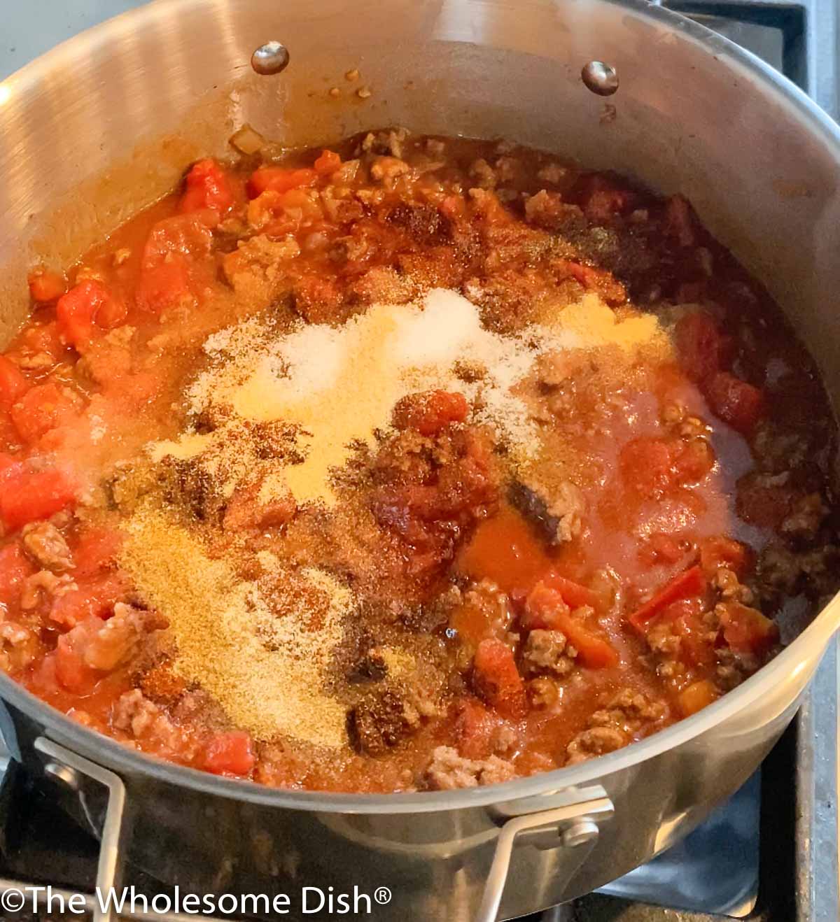 Chili seasonings being added to cooked ground beef and onion in a skillet.