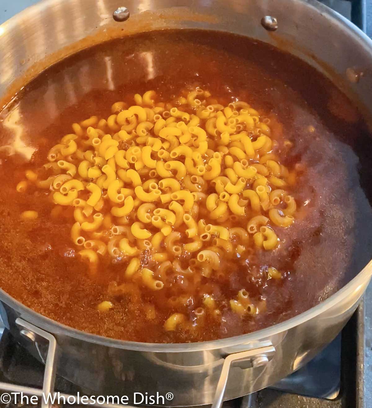 Uncooked macaroni pasta added to chili in a pot.