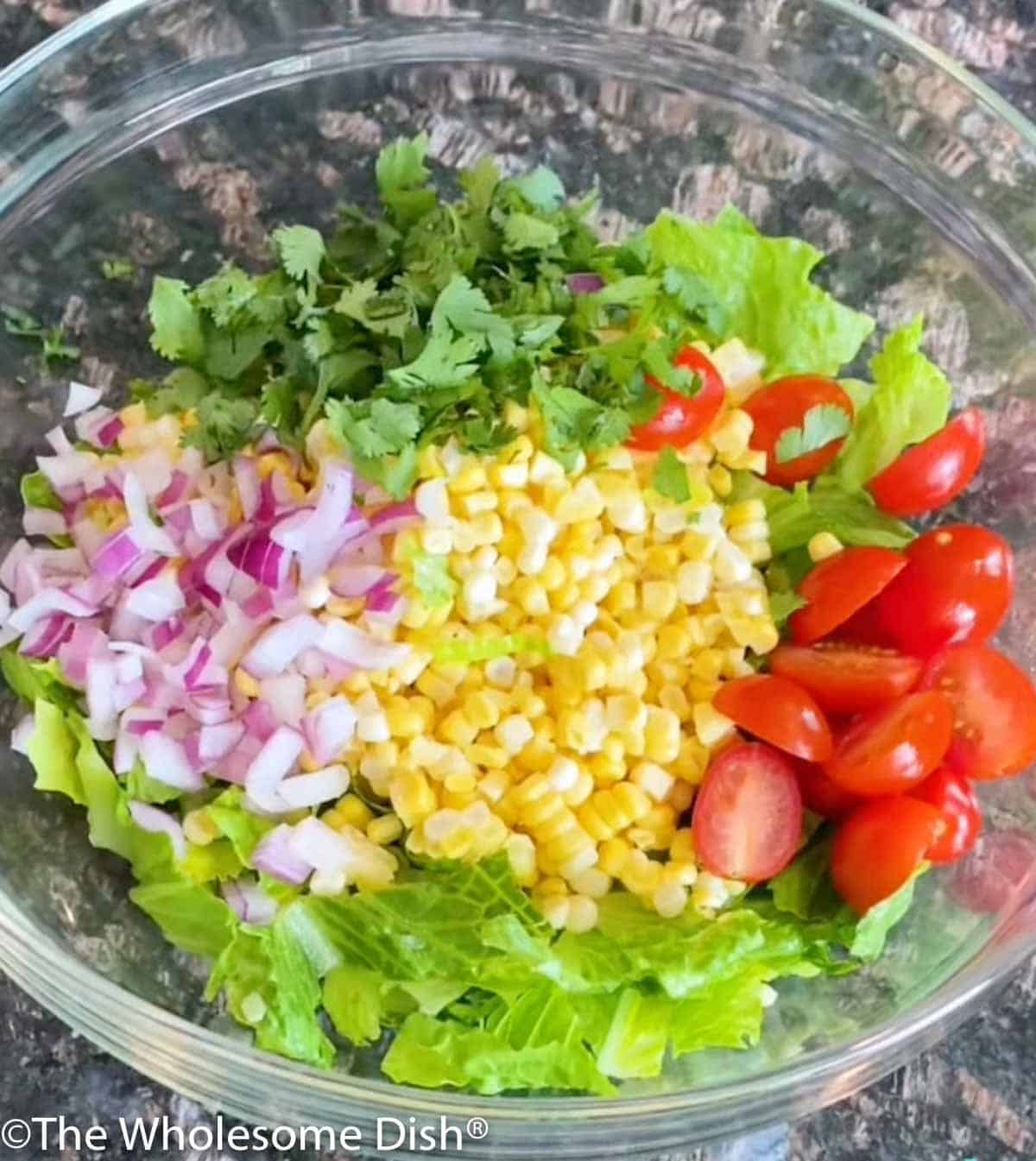 Bowl of chopped lettuce, corn kernels, red onion, and tomatoes.