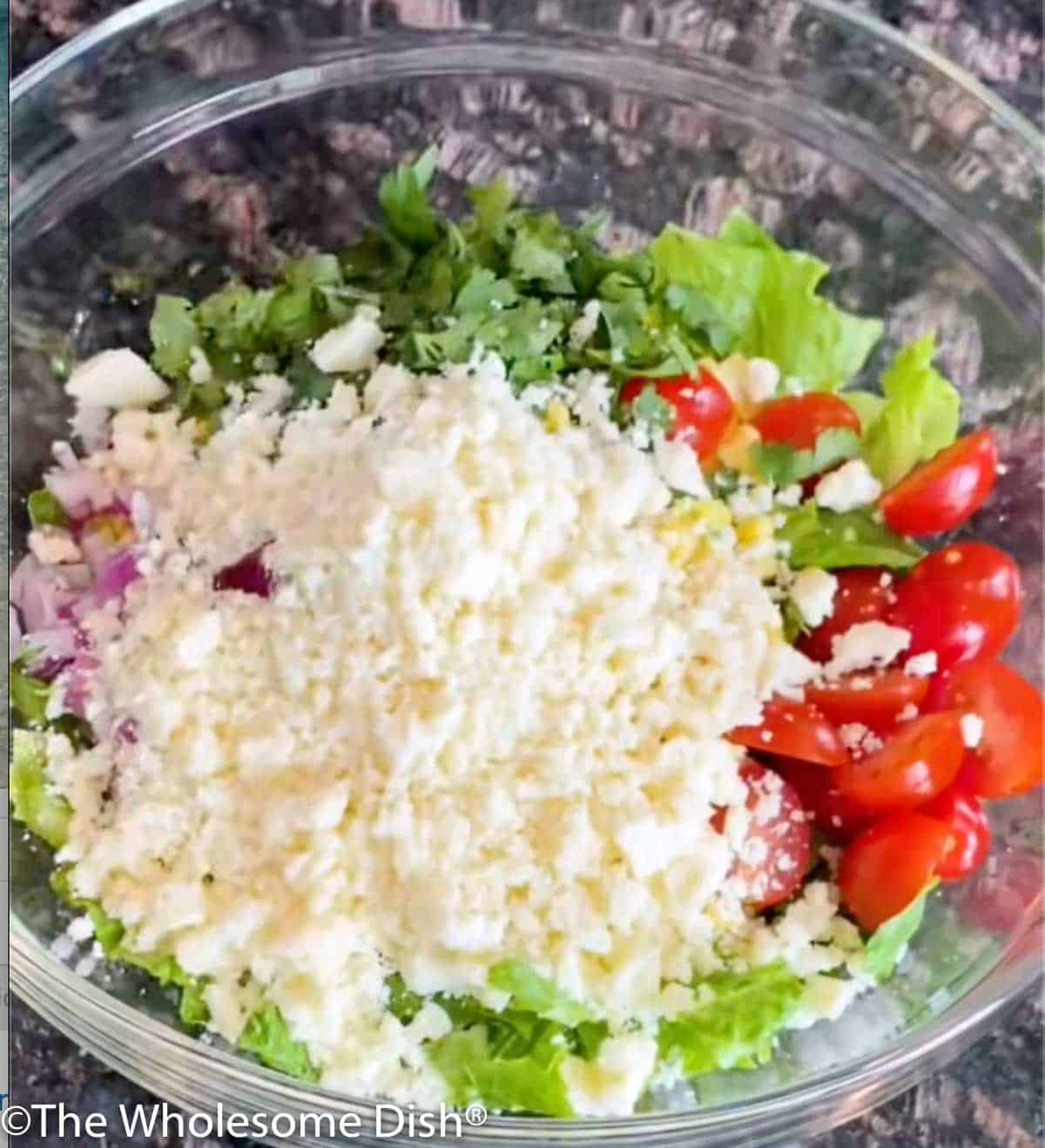 Adding crumbled cotija cheese to a salad.