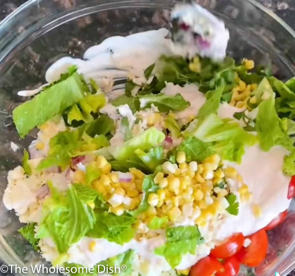 Mixing street corn salad with a creamy dressing.