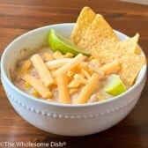 Bowl full of crock pot ranch white chicken chili topped with tortilla chips, cheese, and lime.