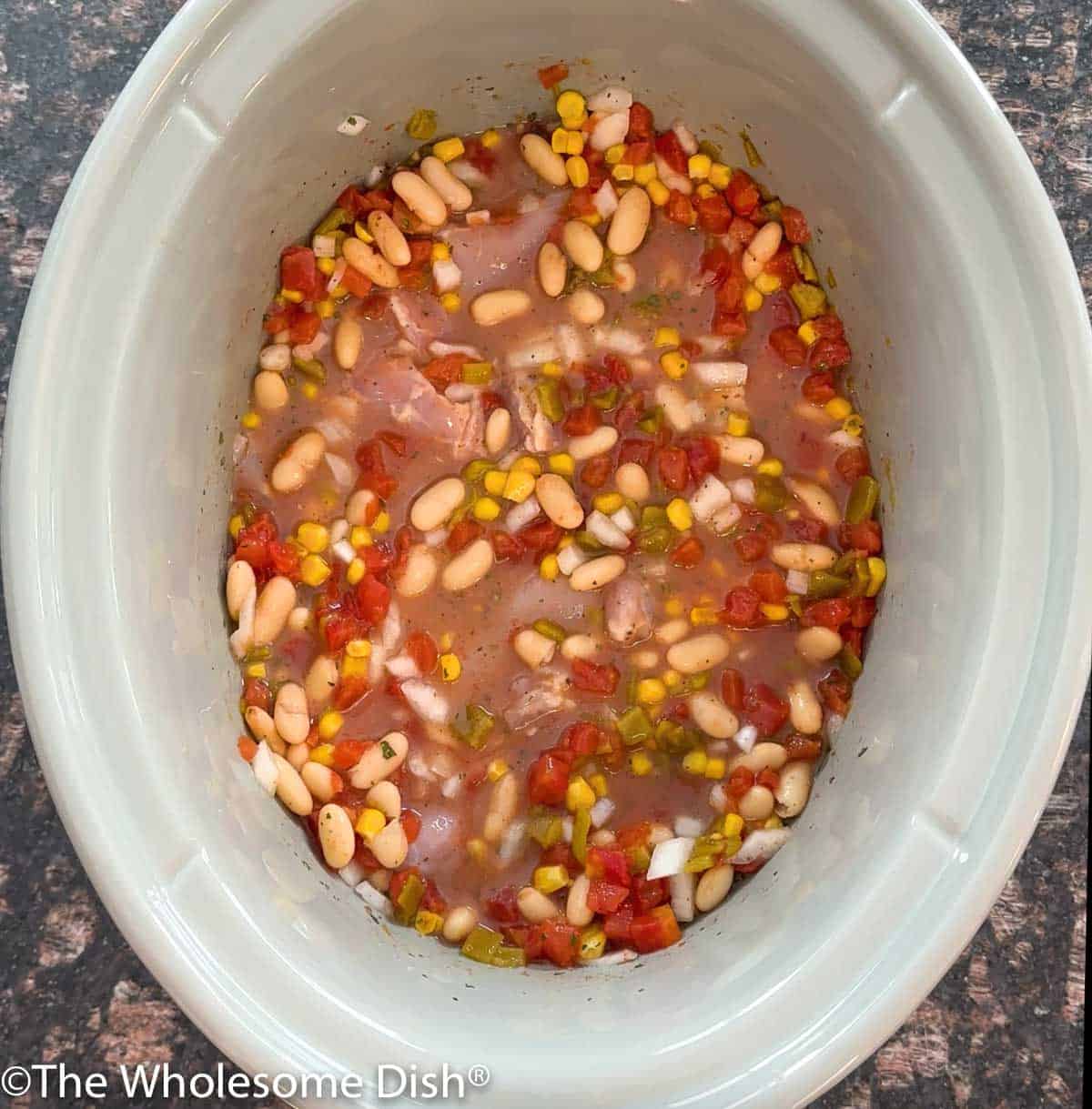 Crock pot with ingredients for ranch chicken chili.