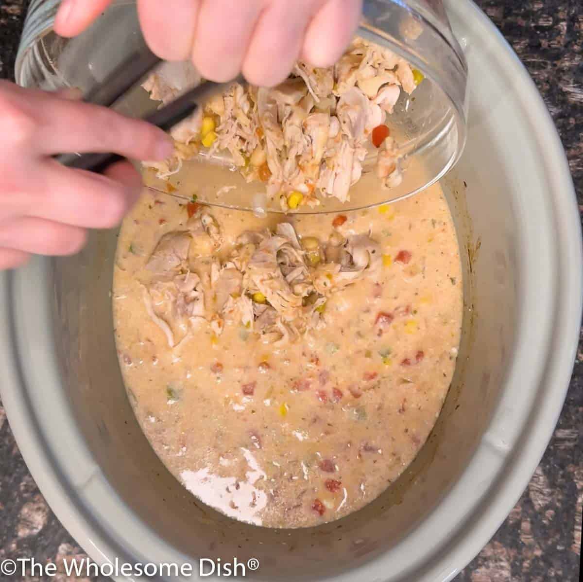 Adding chicken to a slow cooker full of ranch chili.