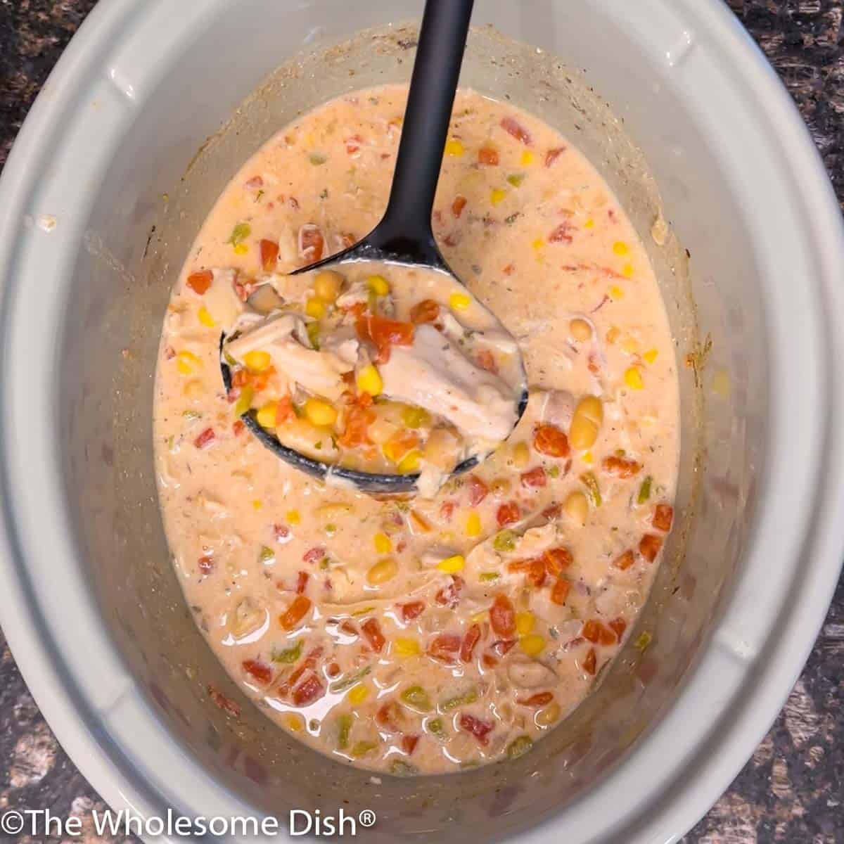 A ladle scooping out ranch white chicken chili out of a crock pot.