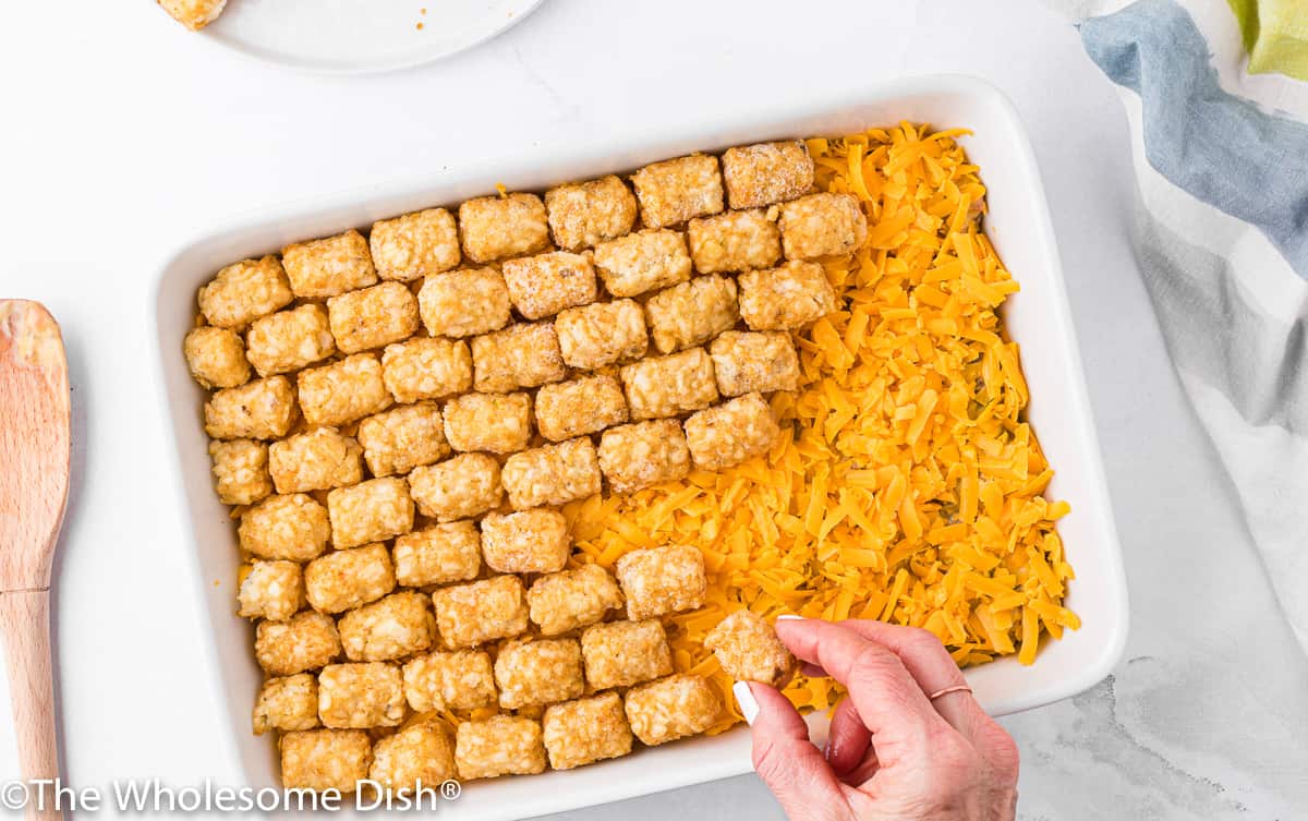 Topping a casserole dish with cheddar cheese and tater tots.
