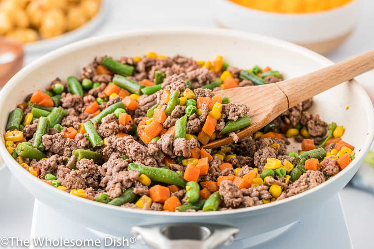 Skillet with hamburger, mixed vegetables, and seasoning.