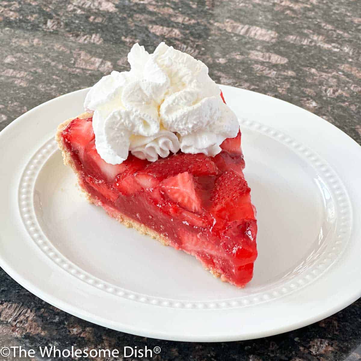 Slice of strawberry jello pie topped with whipped cream on a white plate.