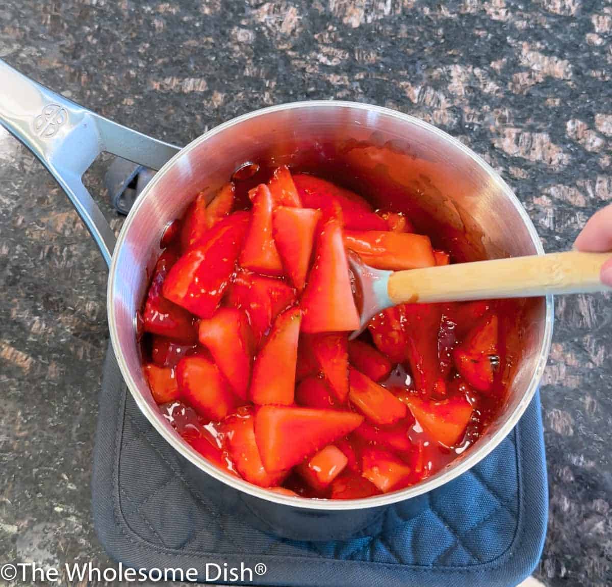 Stirring strawberries into a pot of hot strawberry glaze.