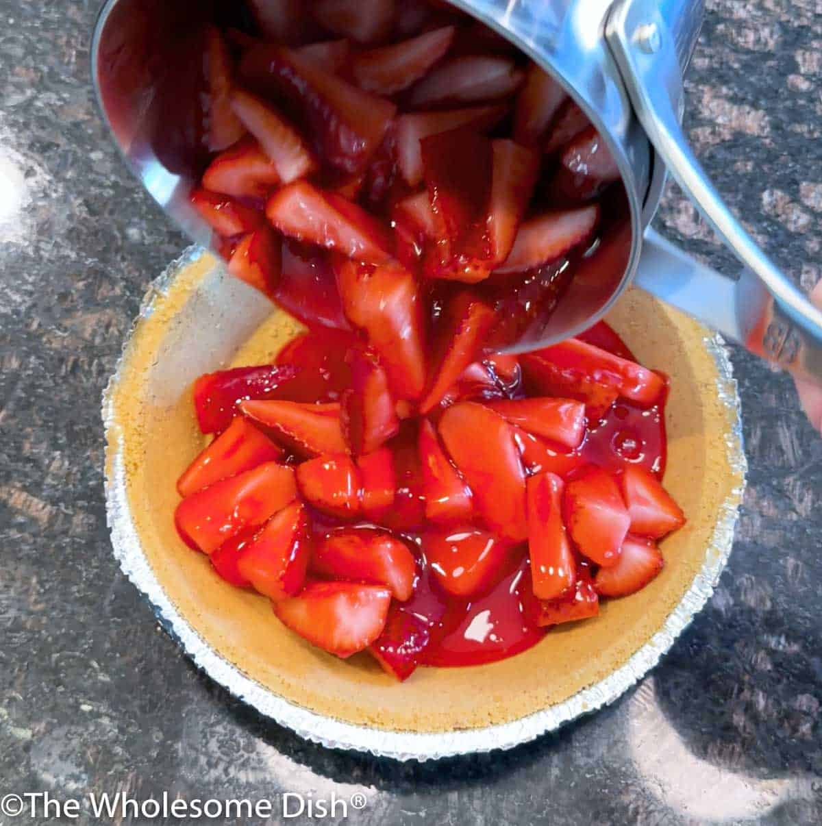 Pouring strawberries coated in sweetened gelatin into a graham cracker pie crust.