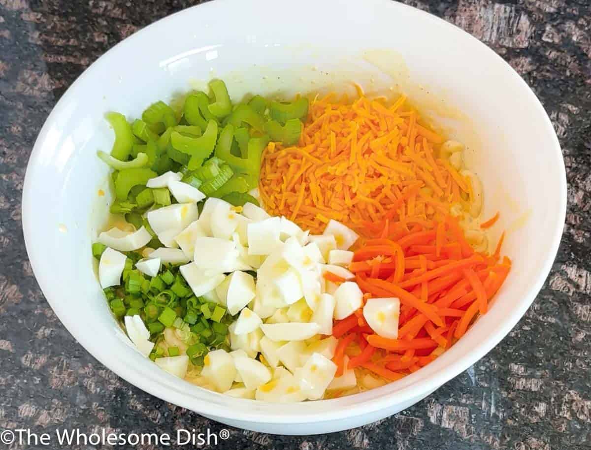 Adding green onions and chopped eggs to macaroni salad.