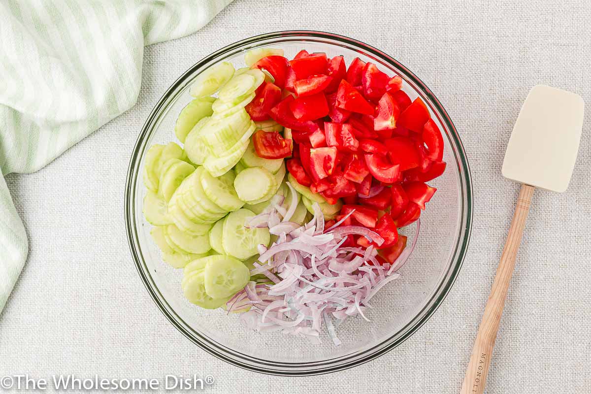 Cucumbers, tomatoes, and red onions in a mixing bowl.