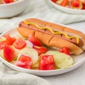 Cucumber salad and a hot dog on a white plate.