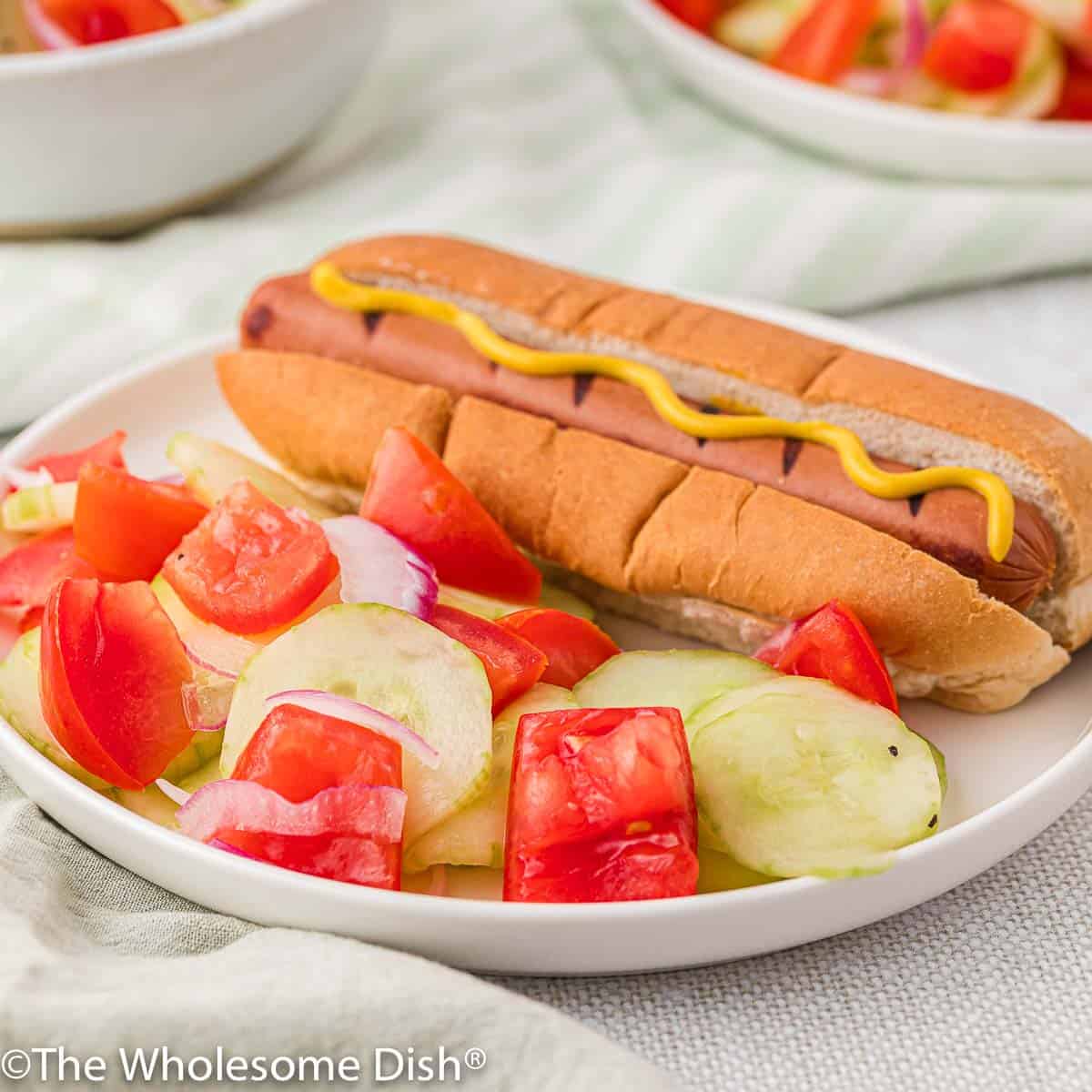 Cucumber salad and a hot dog on a white plate.