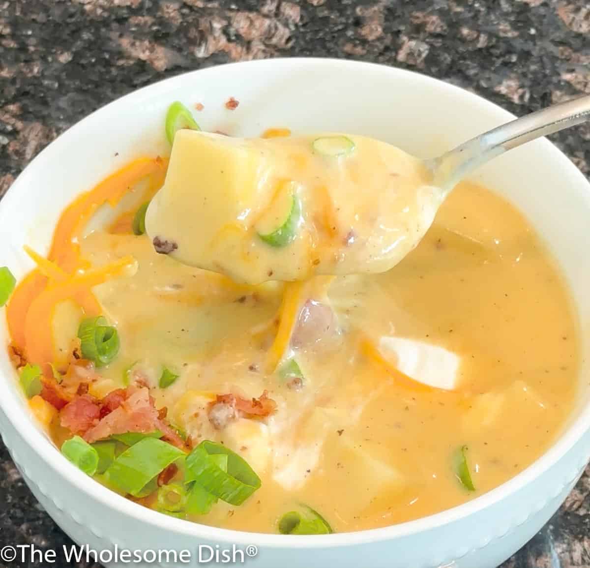 A spoonful of loaded baked potato soup coming out of a white bowl of soup.