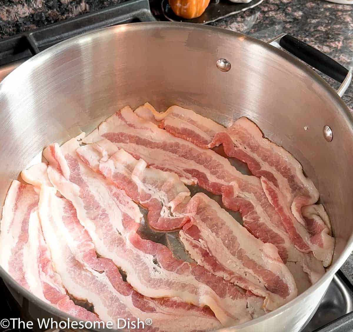 Sliced bacon cooking in a pot.