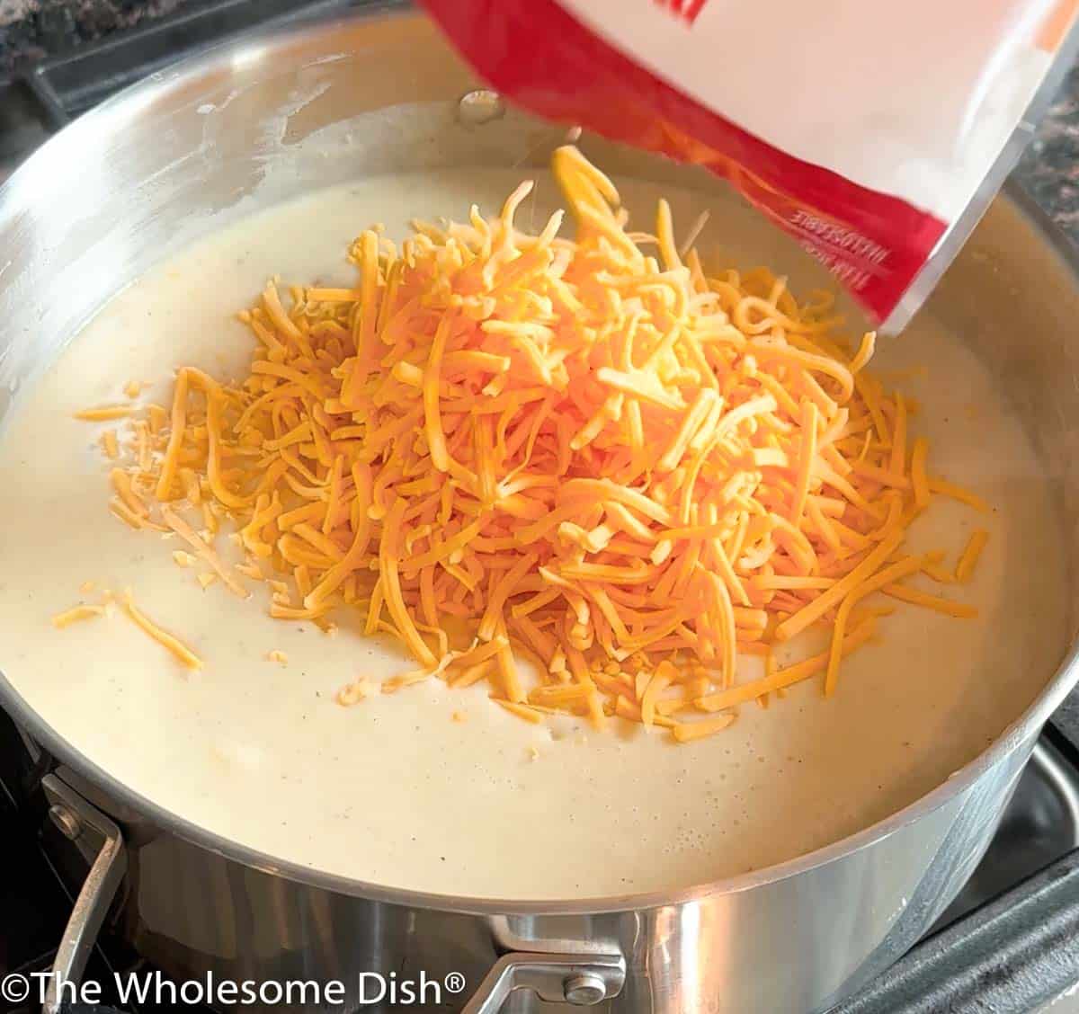 Shredded cheese being added to potato soup in a pot.