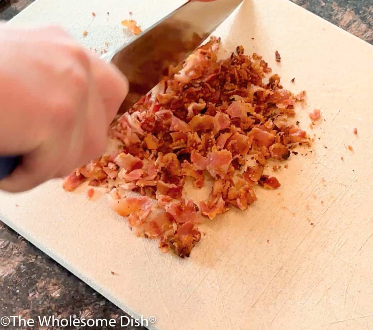 Chopping cooked bacon on a cutting board.