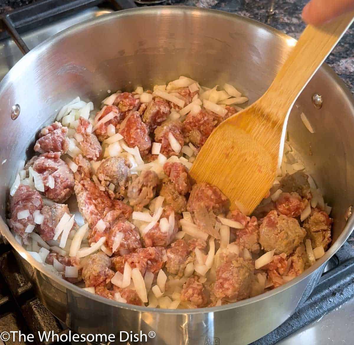 Onion and Italian sausage being cooked in a large pot.