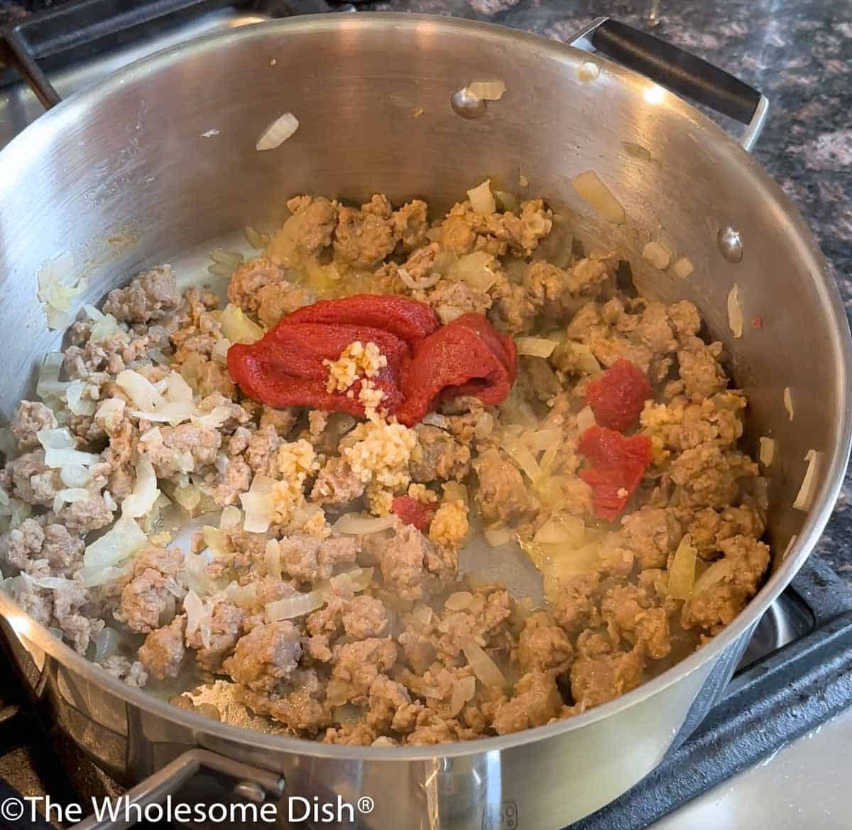 Tomato paste and minced garlic being added to the pot.