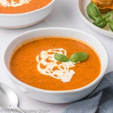 White bowl full of homemade tomato soup topped with cream and basil.