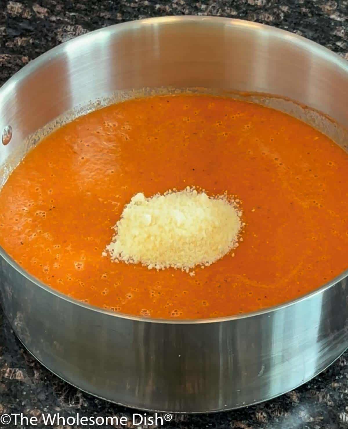 Adding parmesan cheese to the tomato soup.