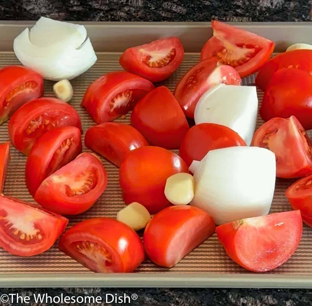 Tomatoes, onion, and garlic cloves on a baking sheet.