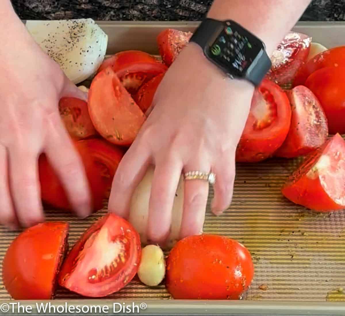 Stirring tomatoes, onion, and garlic with seasoning using hands.