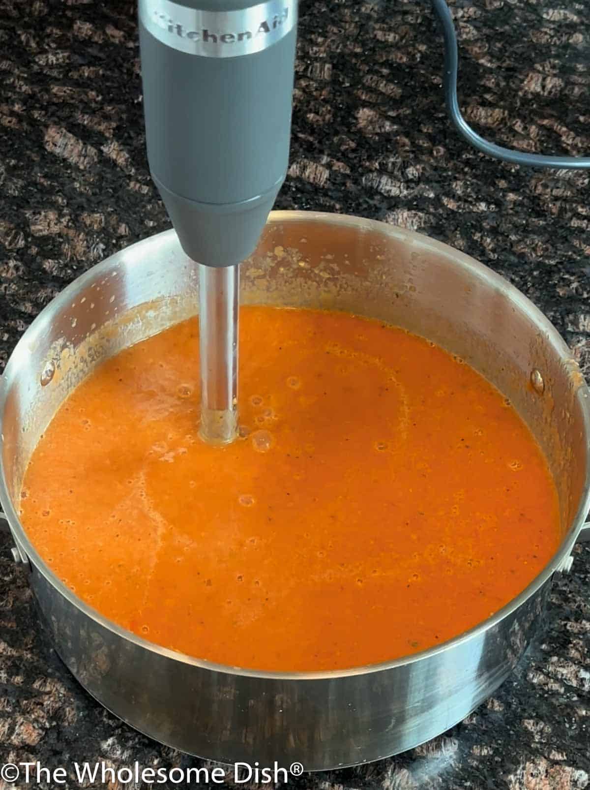 Blending tomato soup with an immersion blender.