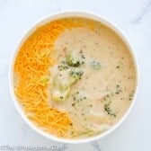Bowl full of broccoli cheddar soup topped with shredded cheddar cheese.
