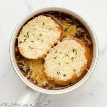 French onion soup topped with bread and melted cheese in a white bowl.