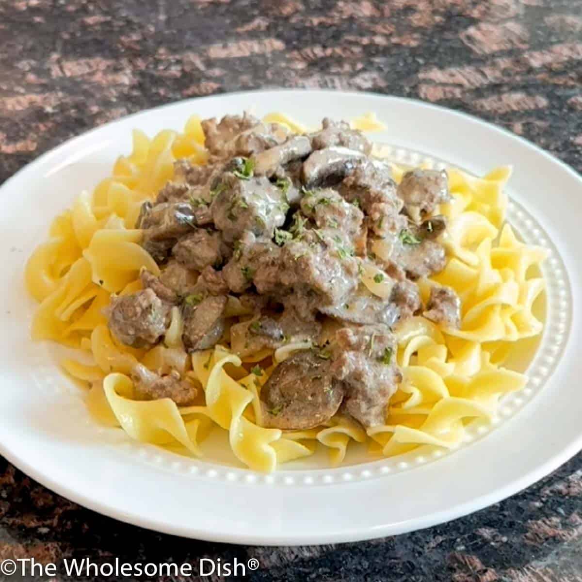 White plate with egg noodles topped with ground beef stroganoff.